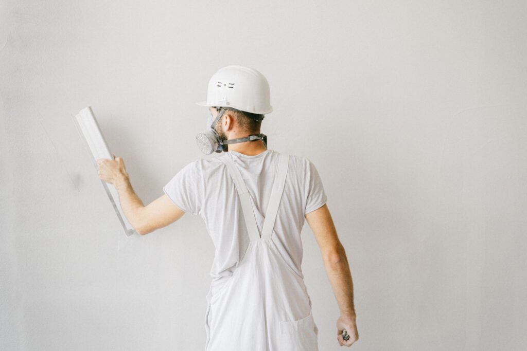 Plasterer in overalls and hard hat finishing a white interior wall