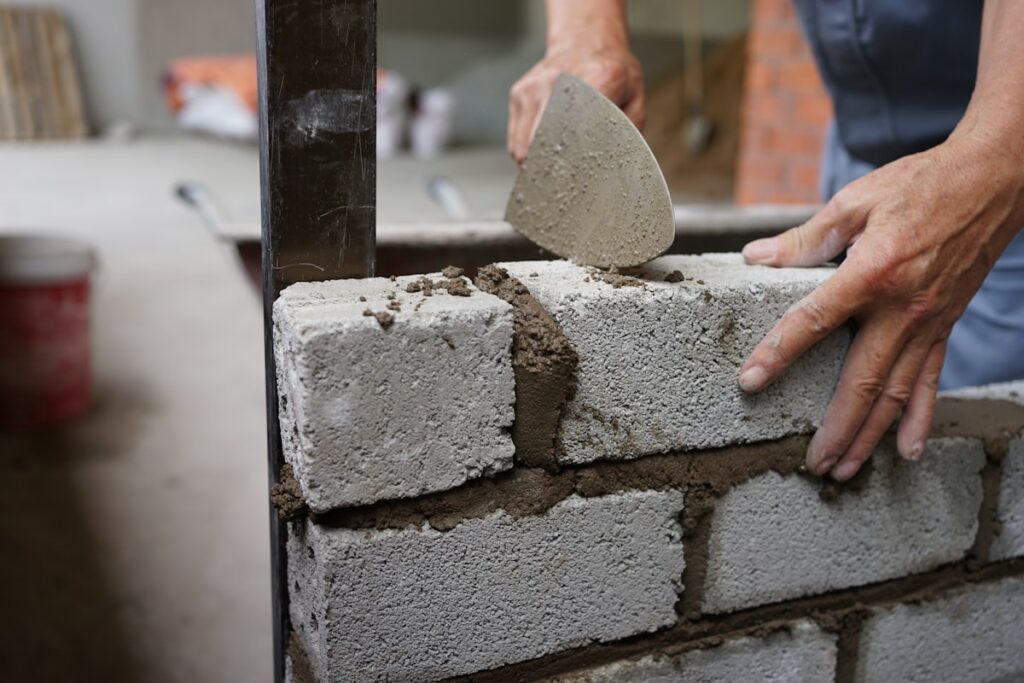 Bricklayer applying cement to a brick wall, representing insurance for bricklayers